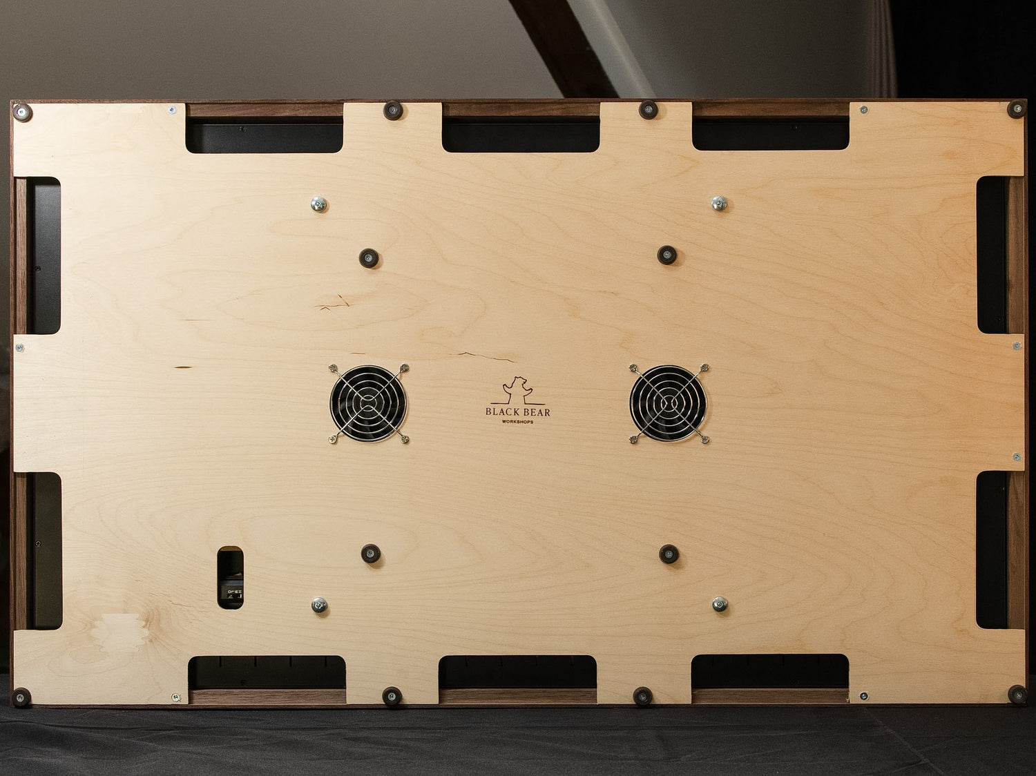 The underside of a digital map case featuring a light natural plywood panel with two black cooling fans, screws, and cutouts, that eradicate heatbox phenomena